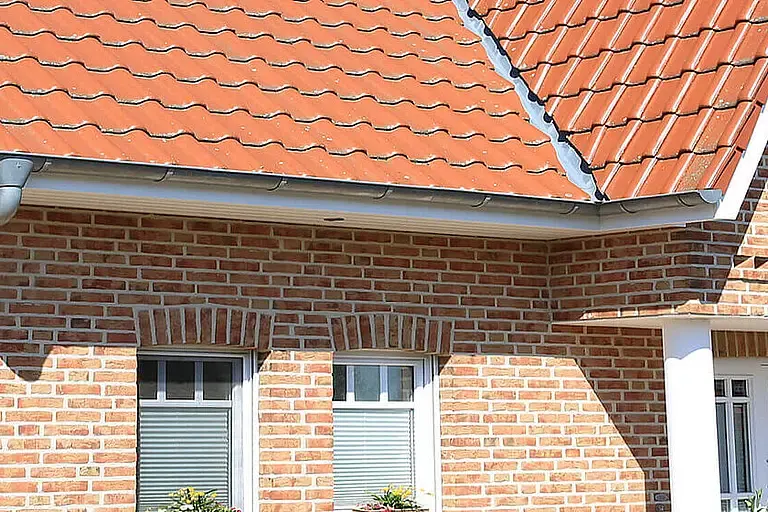 Zweistöckiges Haus aus roten Ziegeln mit weißen Fenstern unter einem roten Ziegeldach